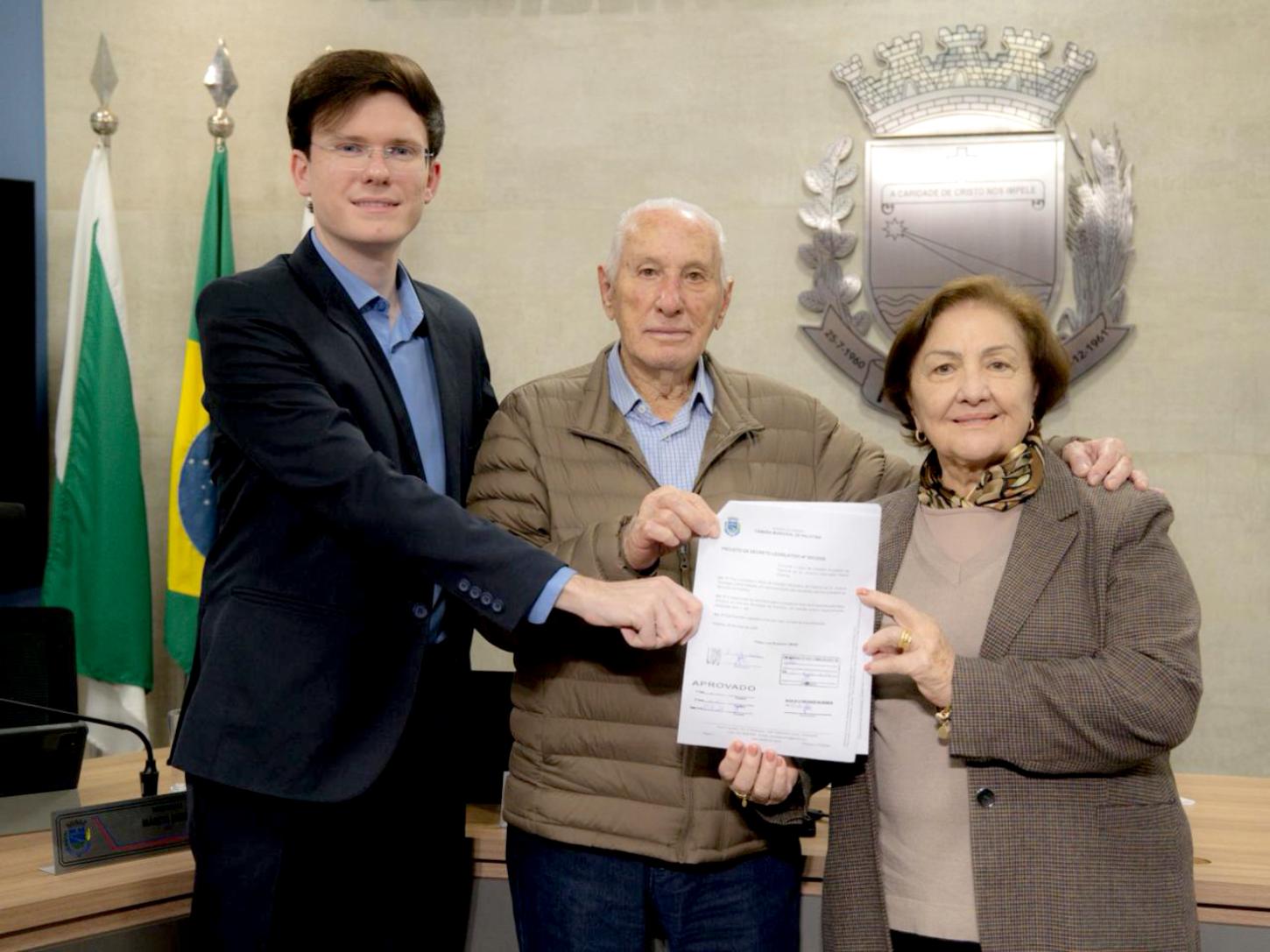 Vereador Filipe Brustolin ao lado do pioneiro Cabral Pelanda e sua esposa, durante registro que marca a aprovação do título de Cidadão Honorário de Palotina